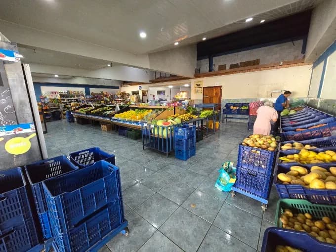 Inside the Hortiluma store: blue crates in the foreground, tables of fruit and vegetables, two people arranging produce.